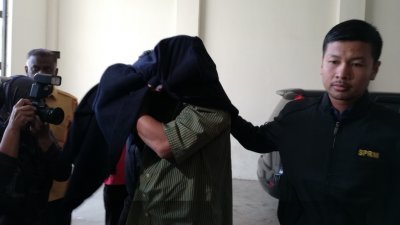 涉滥用特别拨款的前吉打州议员被押上法庭时，以大衣盖住头部，避开摄影镜头。