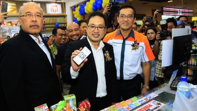张健仁（中）向媒体展示手机中“一触即通”电子钱包。左起为贸消部执法主任 罗斯兰及KK集团创办人兼执行主席蔡志权。