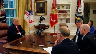 美国总统特朗普（左）周一在白宫椭圆形办公室接受路透社记者专访，右上角为白宫发言人桑德斯。