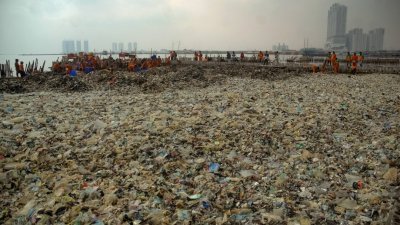 雅加达湾岸边堆满每天被海浪冲上岸的垃圾，与远方的繁华市景形成强烈对比。