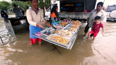 即使水灾来袭，来自关丹双溪依沙达迈花园的苏莱尼（54岁，左），依旧开档售卖炸香蕉与各种糕点。
