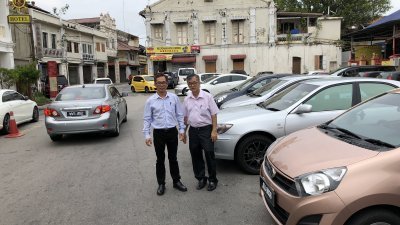刘志良（左）及市议员陈劲源（右）巡视板底街的交通情况，旁为违规停放的车辆。