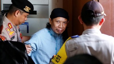 印尼恐怖组织“神权游击队”头目阿曼（中），周五经由印尼法庭判处死刑后，由警员带离法院。