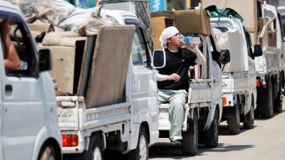 日本冈山县暴雨灾区的民众，周六将受损的家庭用品，送往仓敷市一个临时的废物收集点。当地经历暴雨后，迎来酷热天气，一名青年坐在罗里上休息，补充水分。