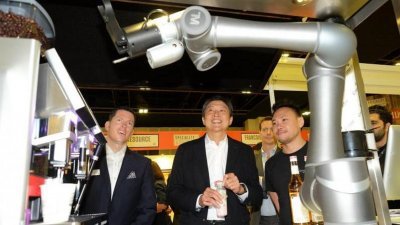机器人咖啡师不但生产力比人手冲泡高5倍，还能用脸部识别技术辨认顾客。黄志明（中）在陈邦耀（右）陪同下，参观这台相信是新加坡首个机器人咖啡师。