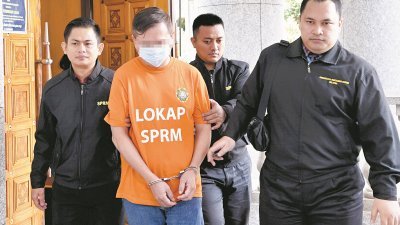 身穿橙色扣留服及戴著手铐的嫌犯在反贪会官员的押送下，抵达布城推事庭。
