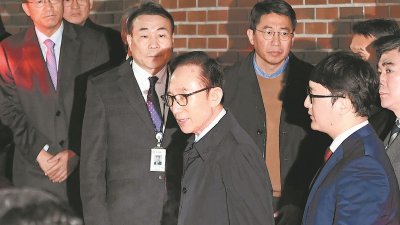 韩国前总统李明博（中）因涉及贪污等罪名，周五凌晨被捕，他在多名检方人员陪同下，步出住所准备乘车前往首尔东部看守所。