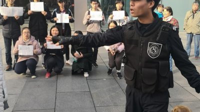 中国学生们在苹果公司北京分店外示威，手持写有谴责苹果工厂非法雇用学生的标语牌。现场有牵著警犬的公安疏散人群。