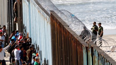 数百中美洲移民抵达墨西哥巴哈半岛与美国加州蒂华纳海滩的边境，有的移民甚至不顾危险，攀上高耸的围栏。美国一边的边境巡防人员，望著围栏另一处的移民们，严阵以待。