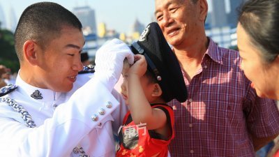 一名华裔警员在结业礼现场与家人分享喜悦同时，也为前来 支持的男童戴上警帽。 （摄影：骆曼）
