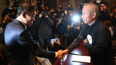 三星电子总裁金奇南（左），周五在首尔韩国新闻中心举行的仲裁案落实协议签字仪式上，与家属代表黄相琪握手。