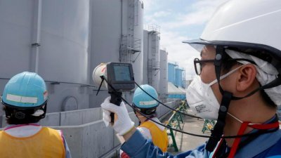 一名东电工作人员，在福岛第一核电厂的辐射污水储水池外，测量辐射值。