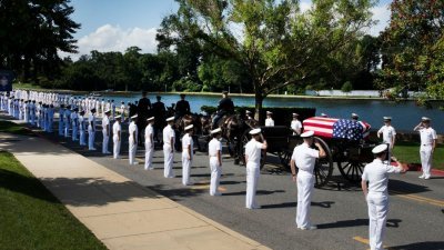 骑著马的军士拉著批有美国国旗的棺木，穿过美国海军学院朝著墓园前进。道路两旁均有身穿白色制服的海军，向麦凯恩敬军礼。