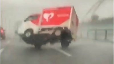 一辆红白相间的货车在公路上行驶途中，遭到狂风暴雨吹得不断往右方向偏，因为风速实在太大了，下一瞬间就然就直间被吹翻。