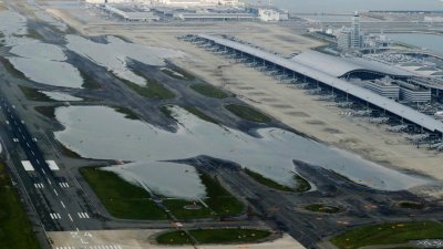 从高空鸟瞰，关西国际机场的跑道在周三仍浸泡在水中。小图为获机场安排搭乘高速船的部分受困旅客，周三抵达神户机场码头。