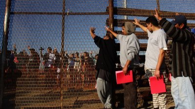 墨西哥的移民在蒂华纳和美国加州圣迭戈边境的双层铁栏前，等候当局放行入境。