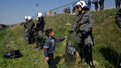 为防移民越境，希腊镇暴警察重兵驻守在季亚瓦塔边界线上。一名移民儿童上前向一名镇暴警察递上鲜花，但对方不为所动。
