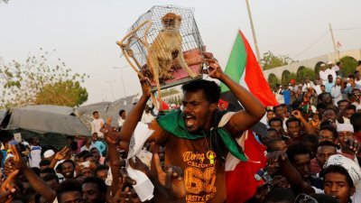苏丹民众在首都喀土穆的国防部前抗议，一名示威者展示一只被绳子绑著被装入笼内的猴子，象征上周被推翻下台的前总统巴希尔，要求当局惩罚他。