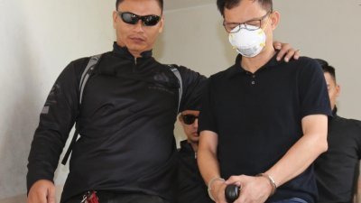 口戴口罩的金金河污染事件涉案新加坡籍男被告（右），周四早上被警方押往新山地庭面控。（摄影：刘维杰）