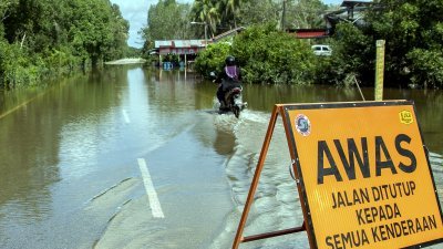 丹州巴西马的洪水仍未退却，当局虽然已关闭当地道路禁止车辆通行，惟仍有部份民众罔顾当局的指示，骑著摩哆涉水而过。