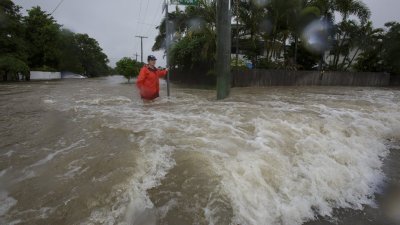 连日暴雨让洪水淹没了昆士兰汤斯维尔市街道，当地居民兰金周日站在水深过膝的洪水中，急湍的洪水几乎将人冲走。