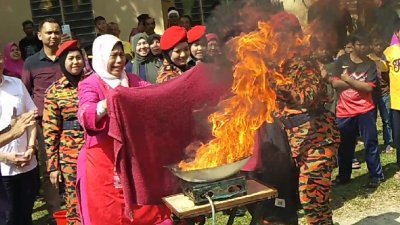 在消拯员教导下，祖莱达（左3）示范若厨具失火时，如何以湿毛巾扑灭火势。