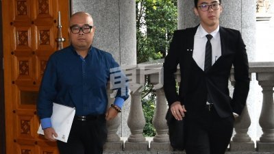李明锭（左）身穿蓝色衬衫，在代表律师陈金福的陪同下，一脸肃穆地步出法庭，毫无回避摄影镜头。