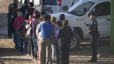 在得克萨斯州的埃尔帕索，一批进入美国遭扣留的非法移民周日在美国海关和边境保护局人员的监督下，排队准备登上当局准备的巴士。