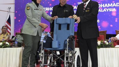 末沙布（中）为军人合作社第54届常年会议主持开幕礼时，见证合作社主席拿督祖基菲里（右）赠送轮椅予该社成员。