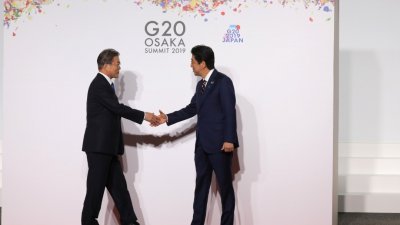 周日在日本大阪举行的G20峰会期间，东道主、日本首相安倍晋三（右）与韩国总统文在寅握手寒暄。日本政府首次对韩国实施经济制裁，被视为日方对韩国政策的方向转变。