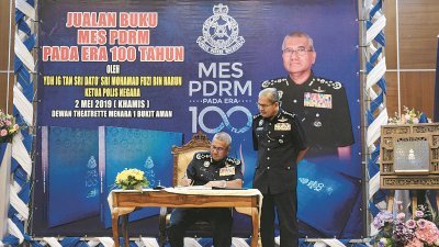 弗兹(左)在出席仪式后，为吉隆坡总警长拿督斯里玛兹兰所购买的“警察100周年特刊”签名留念。