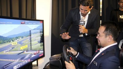 在日前的东南亚电竞赛车大奖赛推介礼上，Axle Motorsport创办人熊龙（站者）向青体部副部长沈志强，展示电竞赛车模拟器的操作方式。