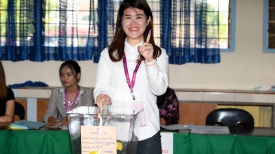 替父亲守土的行动党候选人黄诗琪将选票投入票箱中，并向媒体展示其染墨的食指。