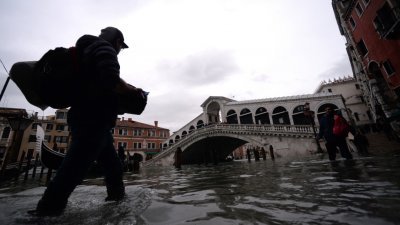 洪水一周内三袭威尼斯，让该城成了名副其实的水都。图为一名男子涉水走过著名里阿尔托桥附近的街道。