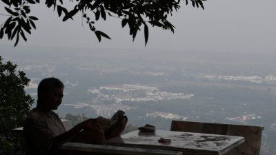 一名浮罗山背居民在一片因烟霾而呈迷濛背景的山上，悠闲看报纸。
