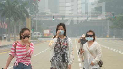 尽管全国空污指数在周六已大有改善，但下午在吉隆坡市区仍一片白茫茫，图为游客戴著口罩在吉隆坡独立广场观光。（摄影：陈启新）
