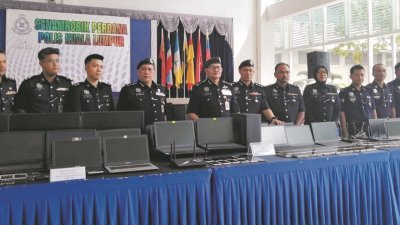 玛兹兰（左五）与建功警官向媒体展示,警方在取缔非法网赌集团呼叫中心时所起获的大批电子器材。