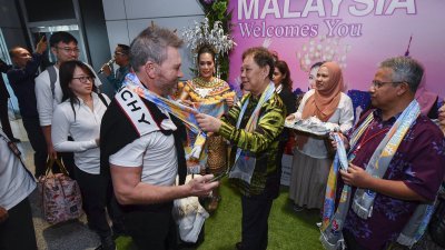 莫哈马丁（中）周三在吉隆坡国际机场，亲自为抵达我国的游客戴上围巾，以表示欢迎来马旅游。