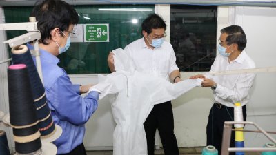 陈天保（左）和林国文（右）向林万锋展示将提交卫生部审核的医用防护衣。