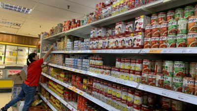 市面上的罐头食品货源充足，一名超市员工在进行日常的补货工作。