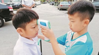 马六甲鼎华华小学生在进入校园前测量体温。