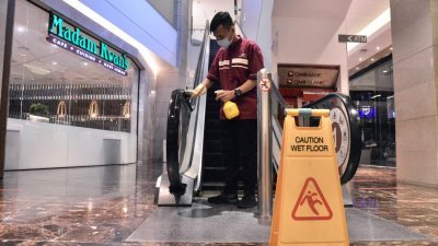 隆雪购物商场如今展开消毒及清洁等工作，准备周一恢复营业。图为一名职员在吉隆坡柏威年广场，为电扶梯等设施进行消毒和清洁，加强防疫。