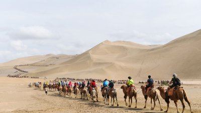 游客骑骆驼在敦煌鸣沙山月牙泉景区游览。（中新社档案照）
