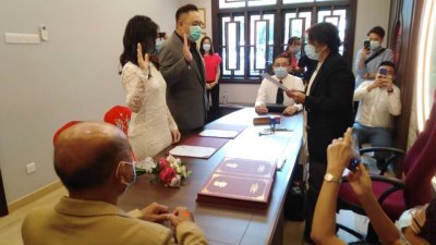 新人李沁燕（站者左起）及杨惟仲在婚姻注册官黄美妹及证婚人的见证下，举手宣誓，注册结婚。