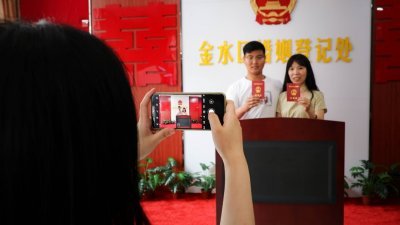 在今年的中国情人节七夕节，大批河南郑州众多新人到婚姻登记处领取结婚证。图为一对新人领证后拍照留念。（中新社）