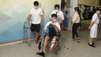 负伤学生在友人的协助下，坐著轮椅到学校上课。