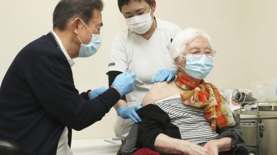 日本中部三重县津市的一个托儿所中，医护人员正为一名中年妇女接种新冠肺炎疫苗。该国自周一起，开始为65岁以上的长者，施打美国辉瑞疫苗。（图取自路透社）