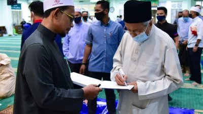马哈迪（右）在出席清真寺祈祷活动后，为支持者在签名簿上签名。
