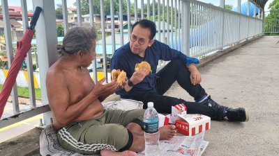 沈志强（右）与一名留宿天桥的街友分享快餐汉堡。