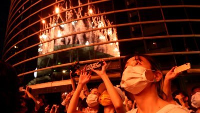 东京奥运会7月23日开幕，由于防疫不开放观众入场，人们在开幕式期间从体育场外观看燃放的烟火。（路透社）